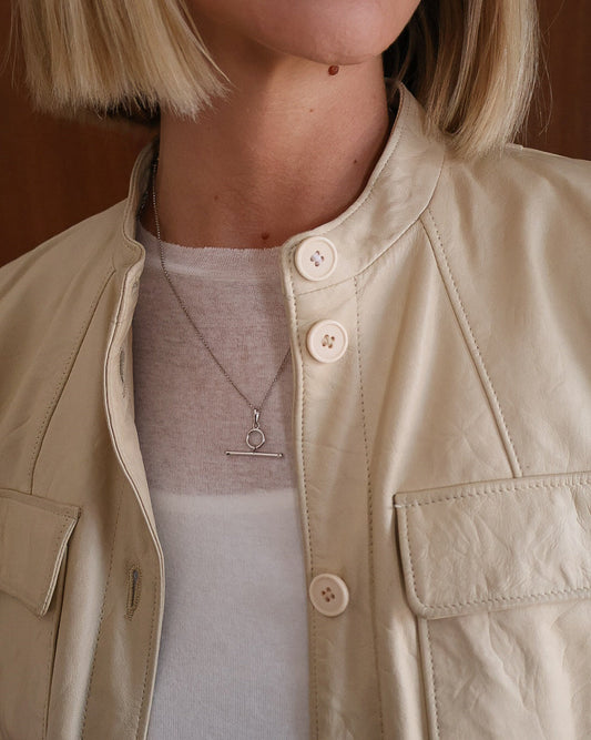 Person wearing a beige jacket with a t bar necklace.